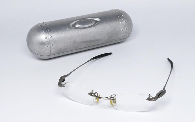 May include: A pair of silver-toned rimless glasses with clear lenses and a silver metal case.