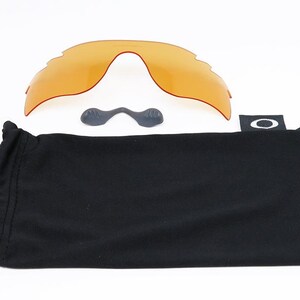 May include: A black microfiber pouch with the Oakley logo, a pair of orange replacement lenses, and two small black nose pads.