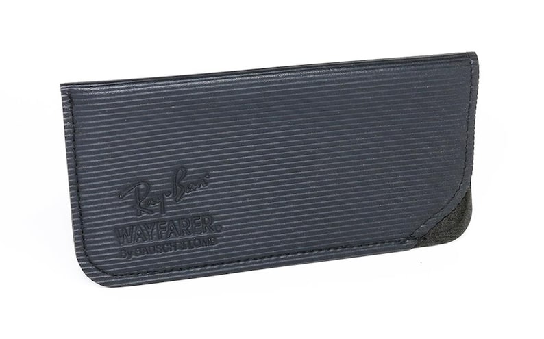 May include: A dark blue Ray-Ban Wayfarer glasses case. The case has a textured, ribbed surface and a black suede corner. The Ray-Ban logo and "WAYFARER BY BAUSCH & LOMB" are embossed on the front.
