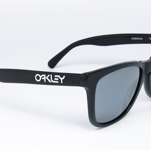 May include: Black Oakley sunglasses with gray lenses. The Oakley logo is displayed in white on the left arm. The sunglasses have a classic, rectangular frame design and are suitable for outdoor activities.