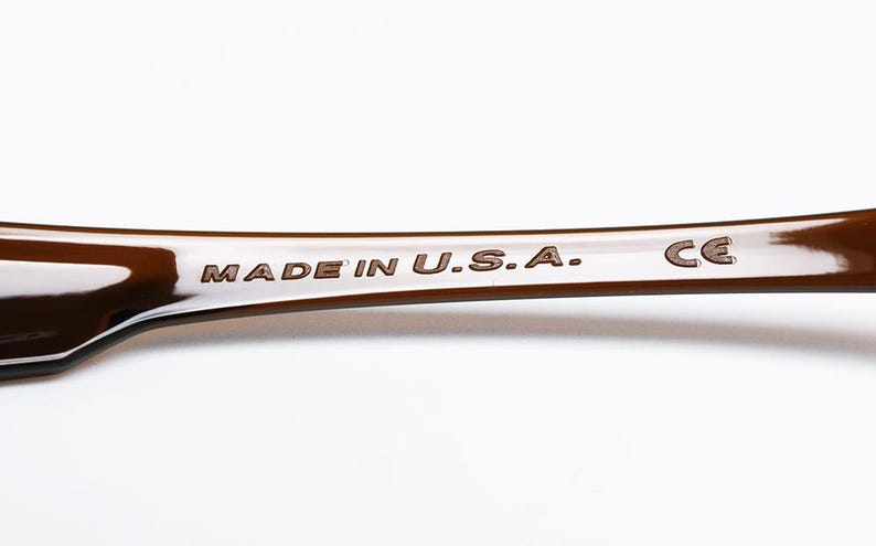 May include: Close-up of a brown, curved object with the text "MADE IN U.S.A." and the letters "CE" etched into the surface. The object has a glossy finish and is set against a white background.