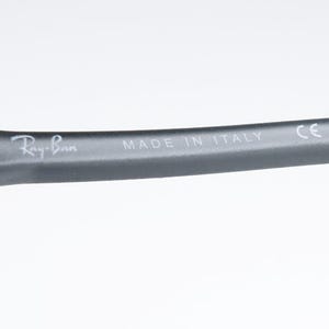 May include: Close-up of a dark gray eyeglass arm with the Ray-Ban logo and the text "MADE IN ITALY". The arm is curved and has a matte finish. The text "CE" is also visible.