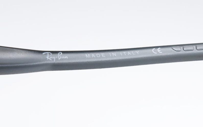 May include: Close-up of a dark gray eyeglass arm with the Ray-Ban logo and the text "MADE IN ITALY". The arm is curved and has a matte finish. The text "CE" is also visible.