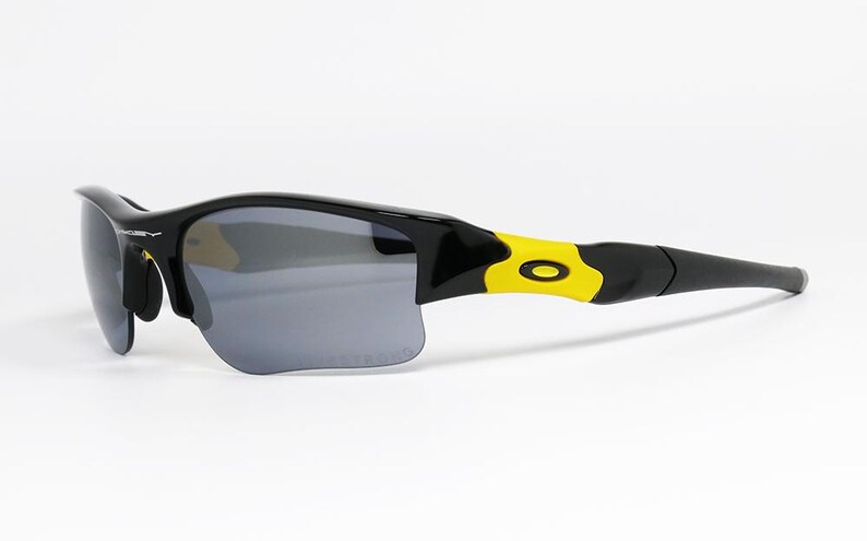 K&ouml;nnte beinhalten: Schwarze und gelbe Sportsonnenbrille mit grauen Gl&auml;sern. Die Sonnenbrille hat ein schlankes, modernes Design mit einem schwarzen Rahmen und gelben Akzenten an den B&uuml;geln. Die Gl&auml;ser sind dunkelgrau und bieten Sonnenschutz.