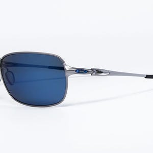 May include: Gray metal sunglasses with blue lenses. The sunglasses have a rectangular frame and a sleek, modern design. The temples are thin and silver, with black ear pieces. The lenses are a deep blue color.