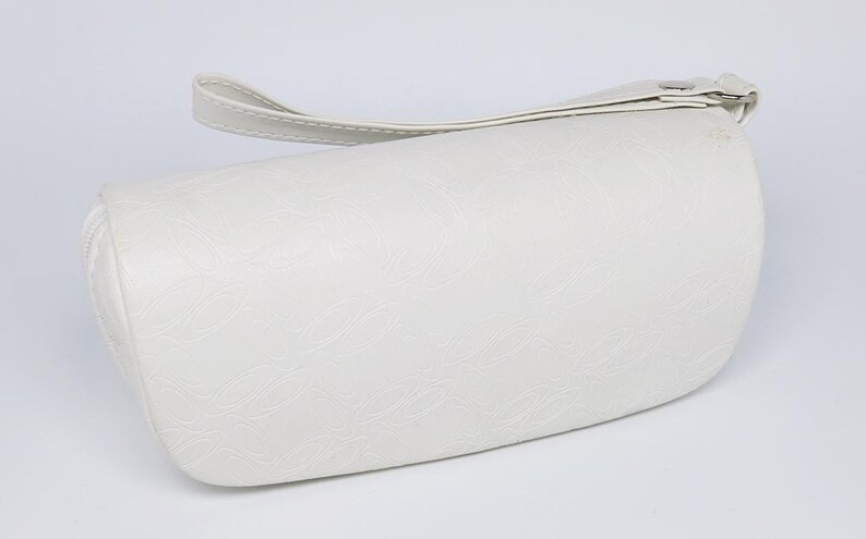K&ouml;nnte beinhalten: Cremefarbene zylindrische Handtasche mit oberem Griff. Die Tasche hat eine strukturierte Oberfl&auml;che mit einem dezenten Wellenmuster. Ein Rei&szlig;verschluss verl&auml;uft entlang der Oberseite. Der Griff ist mit einem Metallverschluss befestigt.