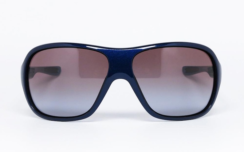 May include: Dark blue sunglasses with a gradient lens. The sunglasses have a thick frame and a rounded shape. The lenses transition from a dark brown at the top to a lighter blue at the bottom.