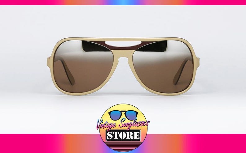 May include: Beige aviator sunglasses with brown gradient lenses. The sunglasses have a thick frame and a bridge detail. The image includes a logo for "Vintage Sunglasses Store" at the bottom.