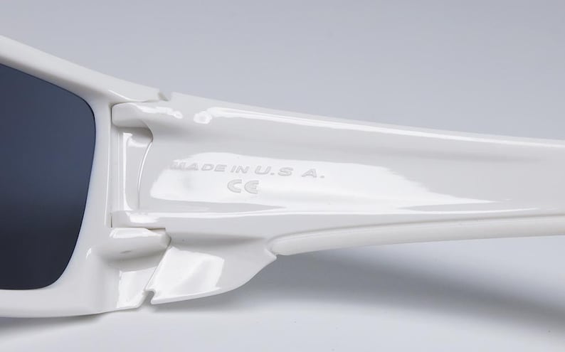 May include: Close-up of white sunglasses with dark lenses. The frame is glossy and features the text "MADE IN U.S.A." and the CE mark. The design is sleek and modern.