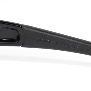 K&ouml;nnte beinhalten: Nahaufnahme des B&uuml;gels einer schwarzen Sonnenbrille mit gelbem Akzent. Der Text "MADE IN U.S.A." ist auf dem B&uuml;gel aufgedruckt.