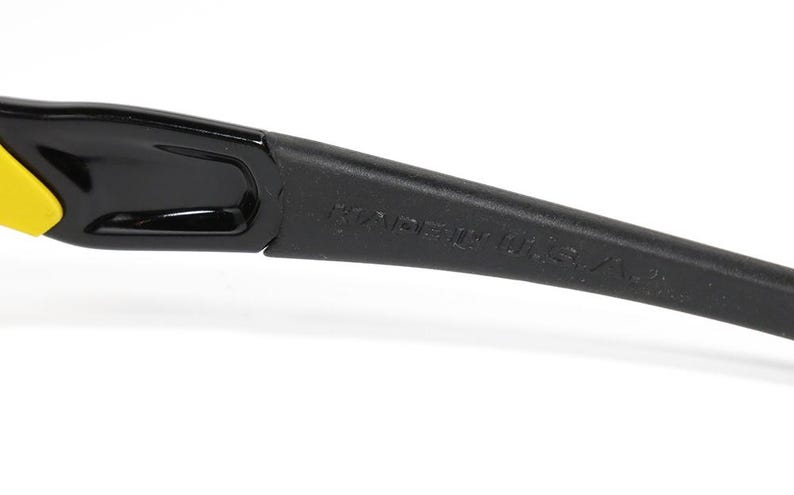 K&ouml;nnte beinhalten: Nahaufnahme des B&uuml;gels einer schwarzen Sonnenbrille mit gelbem Akzent. Der Text "MADE IN U.S.A." ist auf dem B&uuml;gel aufgedruckt.