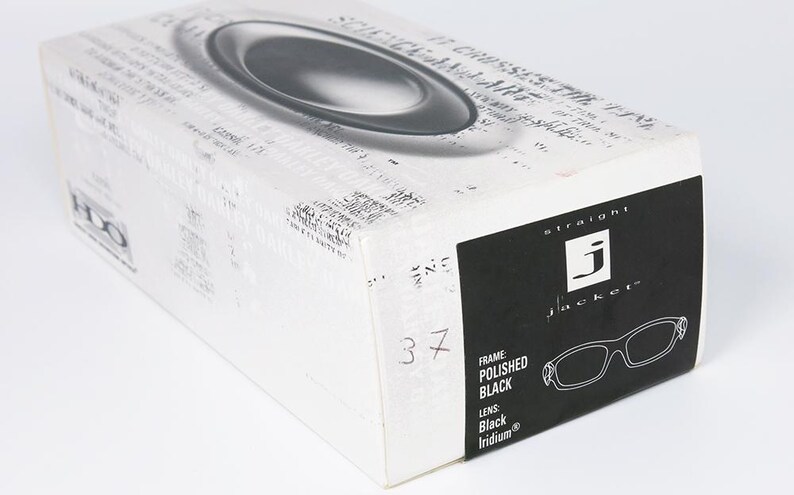 May include: A white and black box for Straight Jacket sunglasses. The box features a black label with the brand name and a drawing of the glasses. The frame is polished black with black iridium lenses. The number 37 is written on the box.
