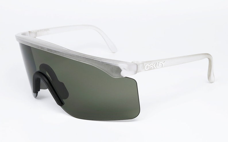 Puede incluir: Gafas de sol con montura transparente y lentes verde oscuro con la palabra "Oakley" impresa en el lateral.