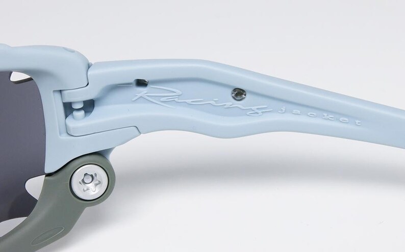 May include: Close-up of light blue sunglasses with the text "Racing jacket" on the arm. The sunglasses have a gray hinge and dark lenses. The frame is a matte finish.