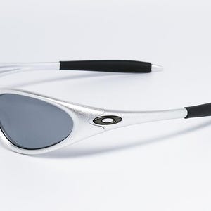 May include: Silver-framed sunglasses with gray lenses. The sunglasses have black temple tips and a small logo on the temples. The design is sleek and modern, suitable for outdoor activities.