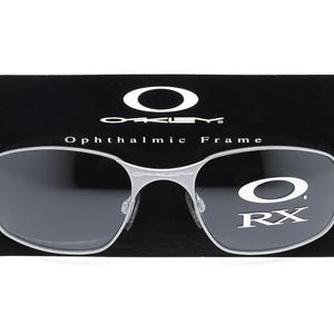 May include: Silver-toned Oakley ophthalmic frame with black lenses and the text "Oakley Ophthalmic Frame RX" on the right lens.