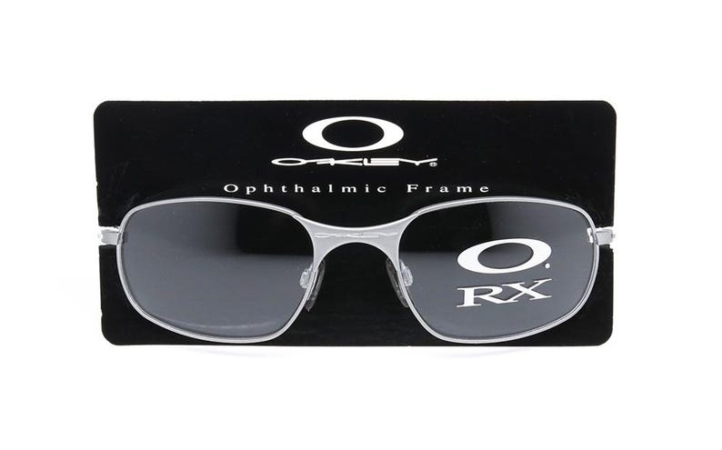May include: Silver-toned Oakley ophthalmic frame with black lenses and the text "Oakley Ophthalmic Frame RX" on the right lens.