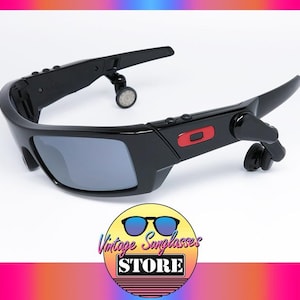 May include: Black sunglasses with gray lenses and a red accent. The sunglasses have a unique design with attached earpieces. The image includes a logo that says "Vintage Sunglasses Store".
