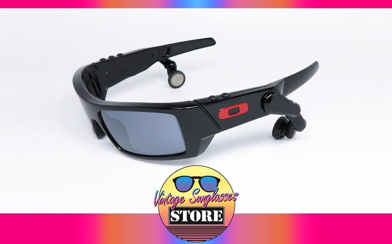 May include: Black sunglasses with gray lenses and a red accent. The sunglasses have a unique design with attached earpieces. The image includes a logo that says "Vintage Sunglasses Store".