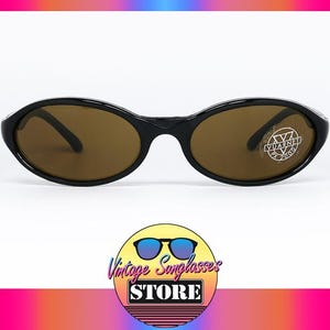 May include: Black oval-shaped sunglasses with brown lenses. The sunglasses have a sleek, modern design. The image includes a logo for a vintage sunglasses store.