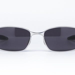 May include: Silver-framed sunglasses with dark gray lenses. The sunglasses have a rectangular shape with rounded edges. The frame is thin and metallic, with hinges on the sides. The lenses are a solid, dark gray color, providing a sleek and modern look.