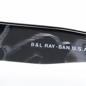 May include: Close-up of the black and gray tortoiseshell frame of a pair of sunglasses. The text "B&L RAY-BAN U.S.A." is printed on the frame.