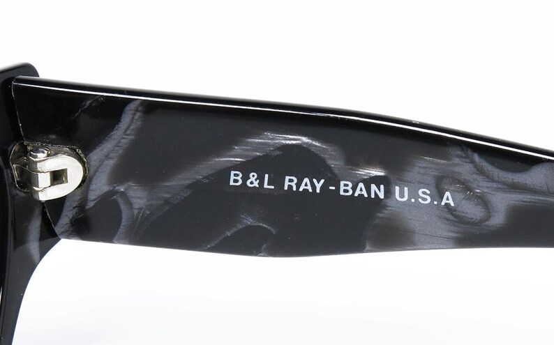 May include: Close-up of the black and gray tortoiseshell frame of a pair of sunglasses. The text "B&L RAY-BAN U.S.A." is printed on the frame.