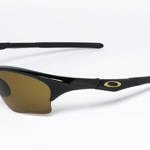 May include: Black sunglasses with brown tinted lenses. The sunglasses have a sleek, curved design with a gold emblem on the temples. The lenses are polarized. The frame is made of a glossy black material.