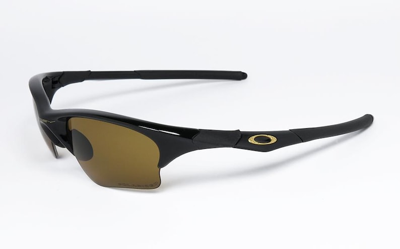 May include: Black sunglasses with brown tinted lenses. The sunglasses have a sleek, curved design with a gold emblem on the temples. The lenses are polarized. The frame is made of a glossy black material.