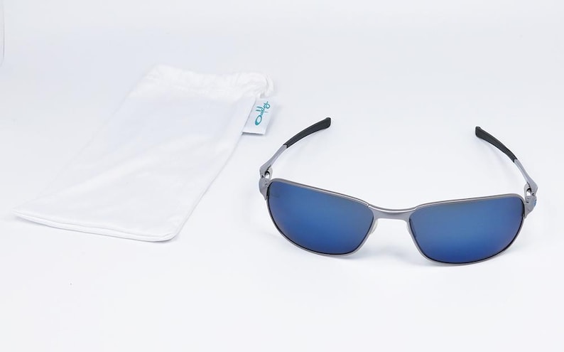 May include: Sunglasses with a silver frame and blue lenses. The sunglasses have black arms and are accompanied by a white drawstring pouch with a small tag. The tag has the word "Oakley" on it.