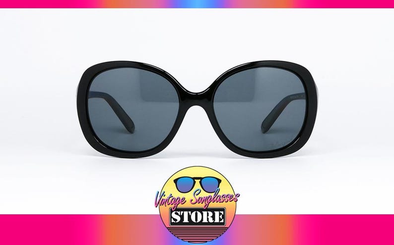 Puede incluir: Gafas de sol negras de gran tama&ntilde;o con lentes de color gris oscuro. Las gafas de sol tienen una montura redondeada en forma de mariposa. La imagen incluye un logotipo que dice "Vintage Sunglasses Store".