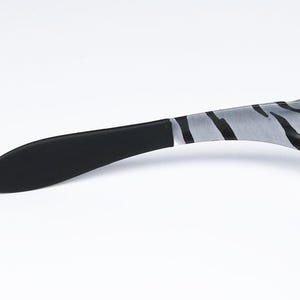 May include: Close-up of sunglasses with a black and white zebra stripe pattern on the temples. The earpiece is black, and the lenses are dark. The sunglasses are set against a white background.