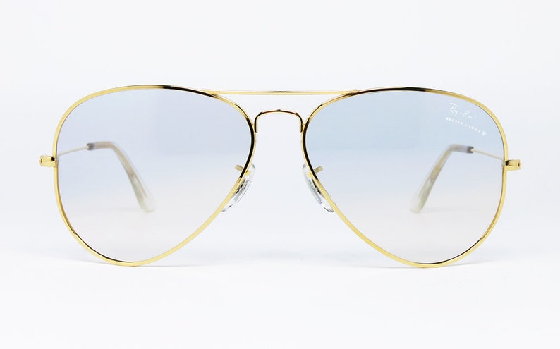 Op de afbeelding: Gouden aviator zonnebril met lichtblauwe gradient lenzen. De zonnebril heeft een Ray-Ban logo op de rechter lens.