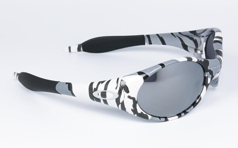May include: Gray and white patterned sunglasses with gray lenses. The frames have a zebra-like pattern in black, gray, and white. The arms have black rubber grips for comfort. A stylish accessory for eye protection.