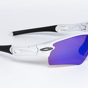 Pu&ograve; includere: Occhiali da sole sportivi bianchi e neri con lenti viola. Gli occhiali hanno un design elegante e moderno con una montatura curva e aste nere. Le lenti sono di un vibrante colore viola.