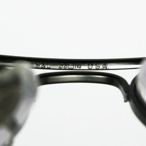 May include: Close-up of the inside of a pair of black eyeglasses with the text "B&L 56□14 USA" engraved on the metal frame.
