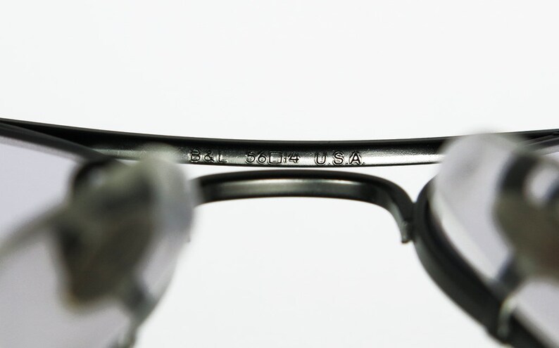 May include: Close-up of the inside of a pair of black eyeglasses with the text "B&L 56□14 USA" engraved on the metal frame.