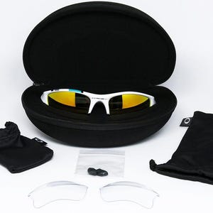 May include: White-framed sunglasses with yellow mirrored lenses rest in an open black case. The image includes a black drawstring bag, a microfiber pouch, a small bag with nose pads, and two clear replacement lenses. The sunglasses are a sporty design.