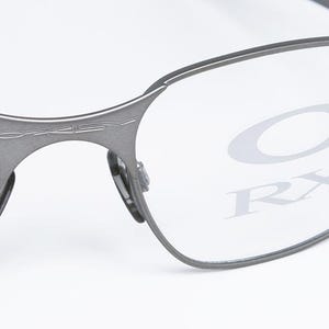 May include: A pair of silver-toned metal frame eyeglasses with clear lenses. The lenses have the Oakley logo and RX printed on them.