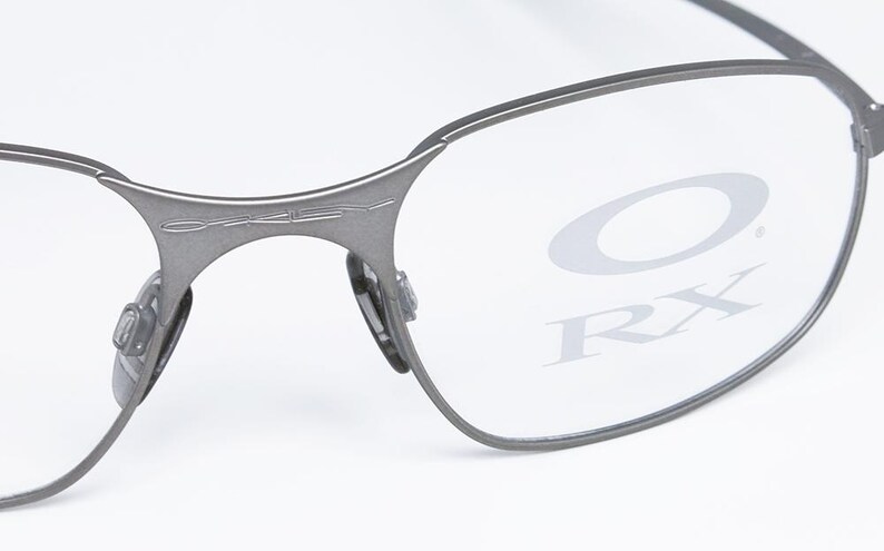 May include: A pair of silver-toned metal frame eyeglasses with clear lenses. The lenses have the Oakley logo and RX printed on them.
