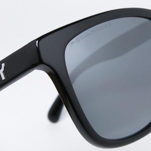 May include: Close-up of black Oakley sunglasses with gray polarized lenses. The Oakley logo is visible on the temple, and the word "POLARIZED" is printed on the lens. The sunglasses have a square frame.