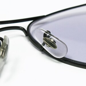 May include: Close-up of black aviator glasses with clear plastic nose pads. The glasses have a light purple tint.