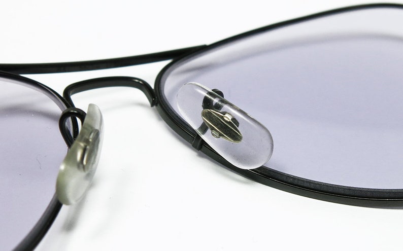 May include: Close-up of black aviator glasses with clear plastic nose pads. The glasses have a light purple tint.