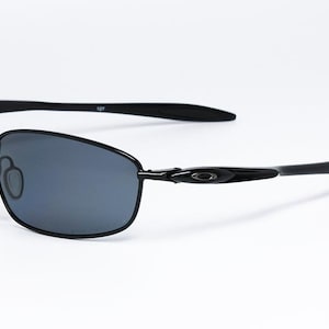 Puede incluir: Gafas de sol negras con un dise&ntilde;o elegante y moderno. Las lentes son de color gris oscuro y las monturas de metal negro. Las patillas se curvan suavemente y las almohadillas nasales son ajustables. Sobre fondo blanco.