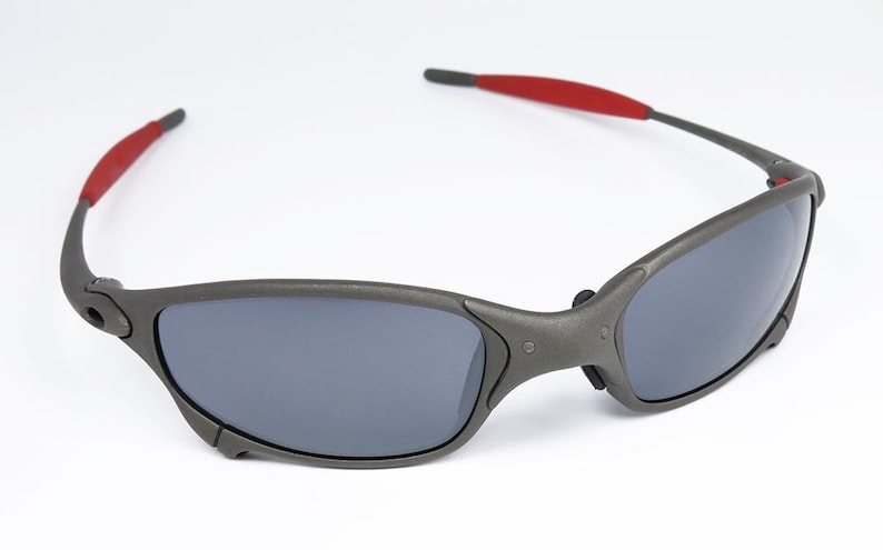 May include: Gray sunglasses with dark lenses and red accents on the temples. The sporty eyewear features a wraparound design and a matte finish, suitable for outdoor activities and everyday wear.
