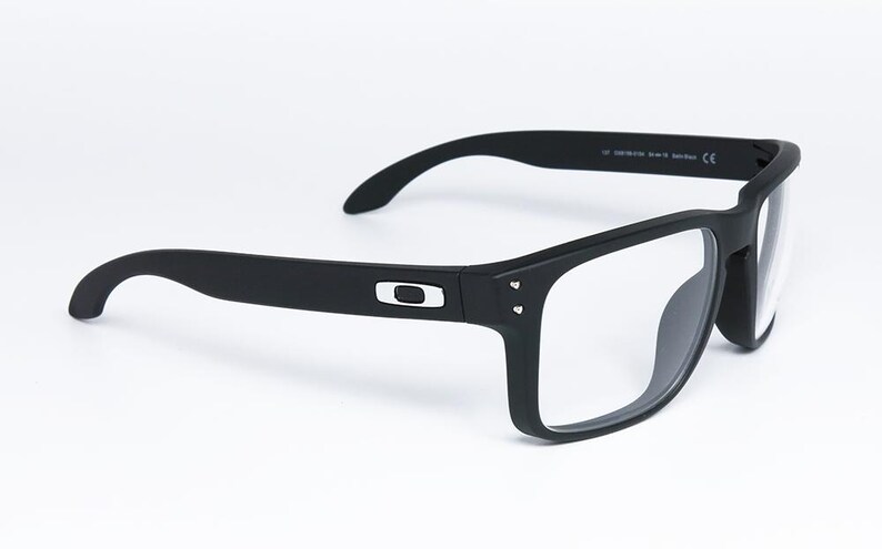 May include: Black rectangular eyeglasses with clear lenses. The frames are matte black with a silver logo on the temples. The glasses have a modern, sporty design, suitable for everyday wear.