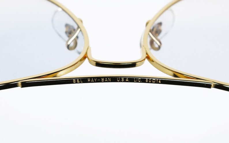 Op de afbeelding: Close-up van de inscriptie op de poot van een paar gouden aviator-zonnebrillen. De inscriptie luidt "B&L RAY-BAN U.S.A. LIC. 60014".