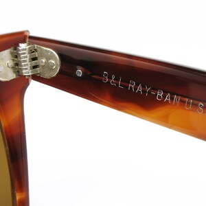 Peut inclure: Gros plan sur la charni&egrave;re et la branche d'une paire de lunettes de soleil Ray-Ban en &eacute;caille de tortue brune. La branche est grav&eacute;e "B&L RAY-BAN U.S.A."