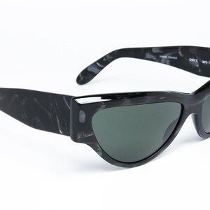 May include: Black and white marbled sunglasses with a cat-eye shape and green lenses. The sunglasses have the text "ONYX  WO 738" on the side.