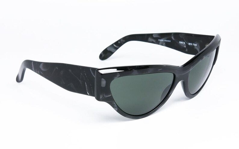 May include: Black and white marbled sunglasses with a cat-eye shape and green lenses. The sunglasses have the text "ONYX  WO 738" on the side.